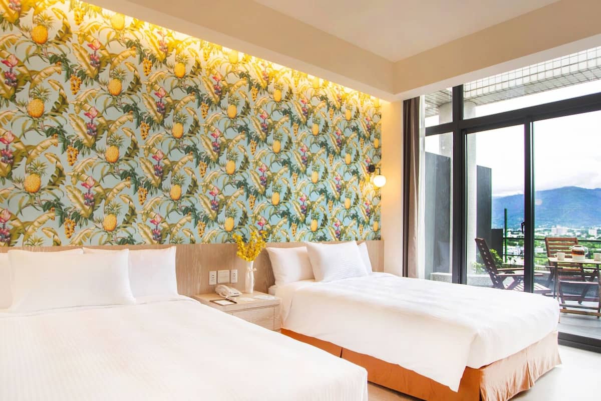 Habitació d'hotel amb dos llits, una finestra gran amb vista a la ciutat i un paper pintat amb temàtica tropical.