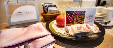 A table with a calendar, a plate with a red apple, a napkin, a pair of scissors, a plate with a card, and a basket with food items.