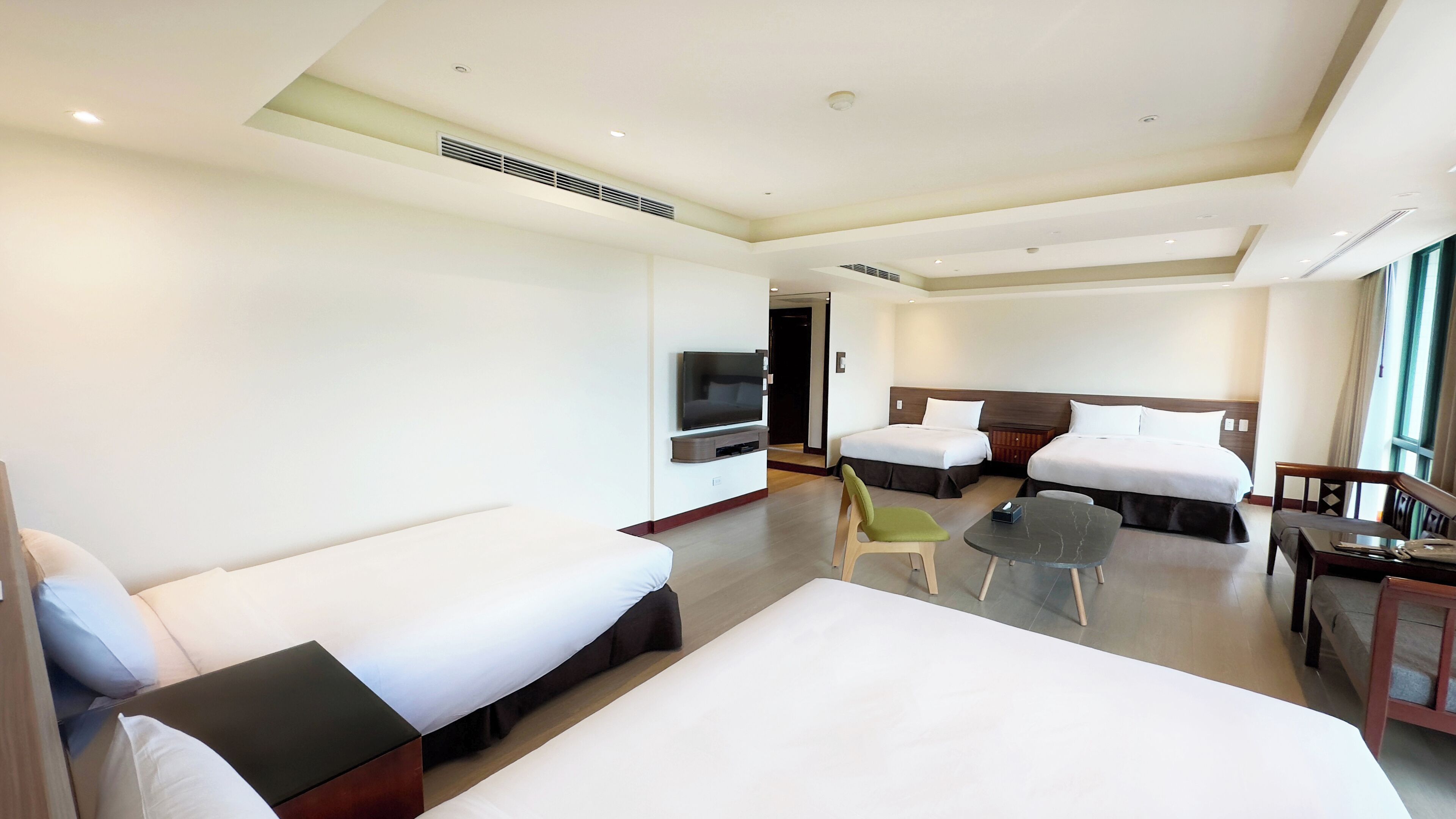 A hotel room with two single beds, a sofa, a TV, a small table, and a chair.