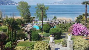 A view of a resort with a pool, palm trees, and a mountain backdrop. - Wellness & Beauty Hotel Conca Azzurra (Ranco)