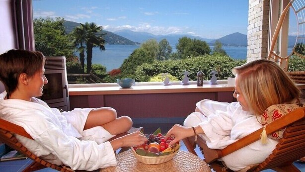 Two people sitting on wicker chairs facing a balcony with a view of a lake and mountains. - Wellness & Beauty Hotel Conca Azzurra (Ranco)