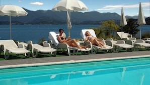 A poolside area with lounge chairs and umbrellas, a clear sky, and a mountainous backdrop. - Wellness & Beauty Hotel Conca Azzurra (Ranco)