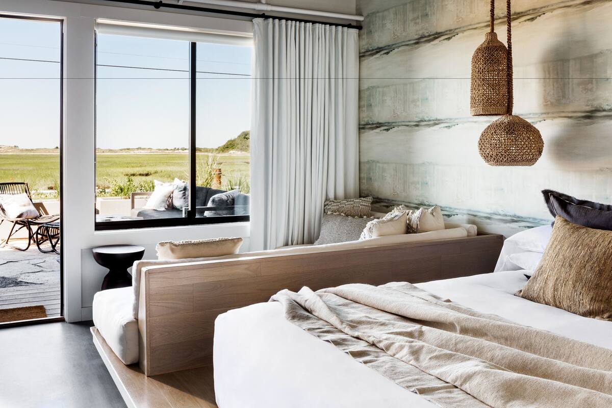 A bedroom with a large window, a bed, a sofa, and a hanging light fixture.