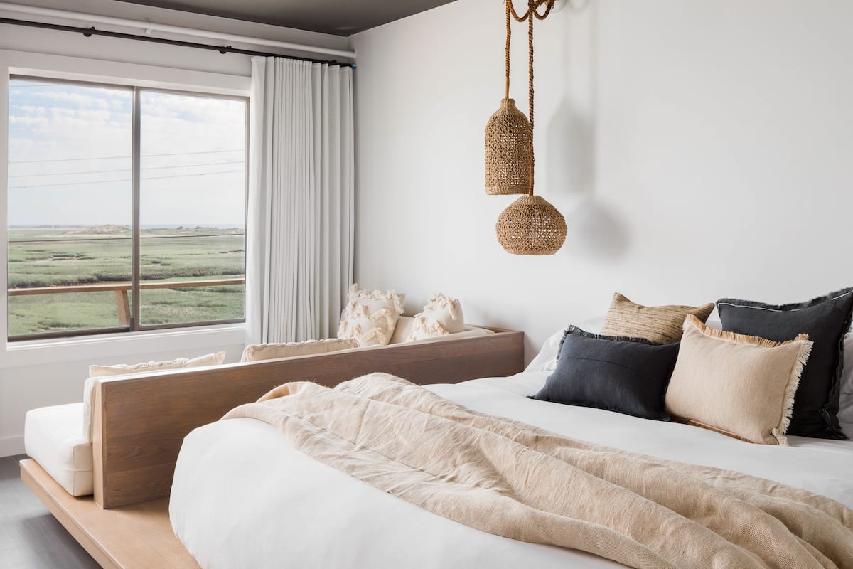 A bedroom with a large bed, a view of a field through a window, and a hanging light fixture.