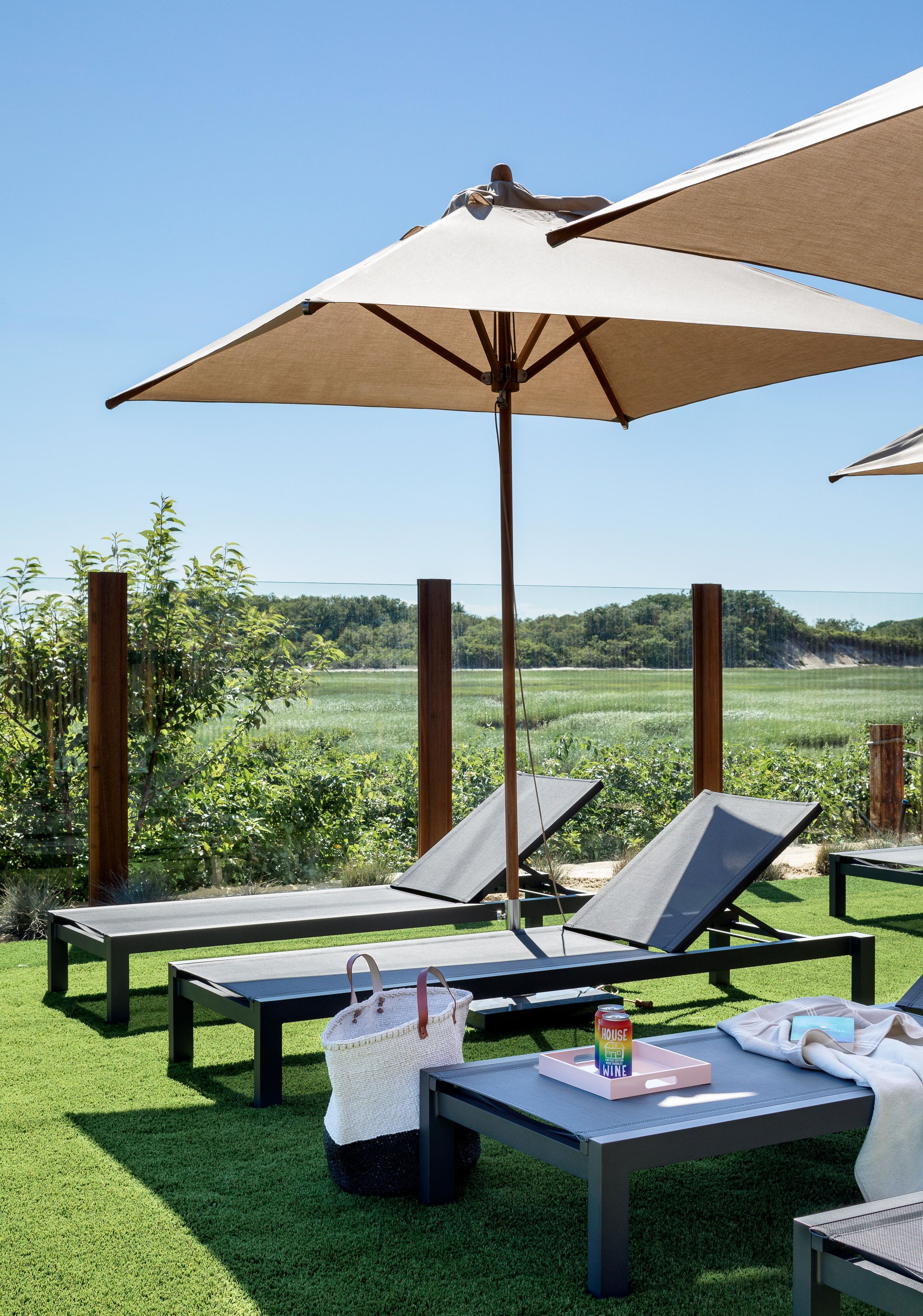 Zona junto a la piscina con sillones de descanso, una mesa con posavasos para bebidas y una sombrilla grande que da sombra.