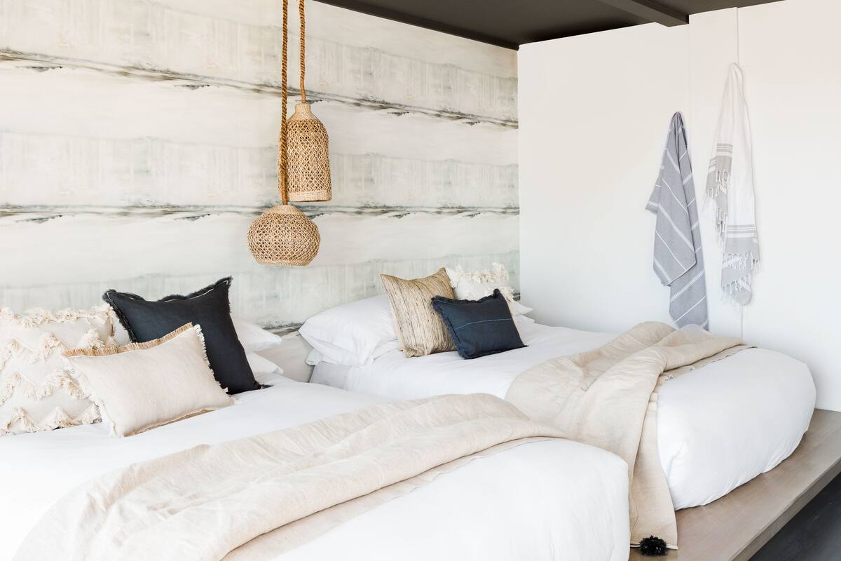 A bedroom with two beds, a hanging woven light fixture, and a wall-mounted towel rack.