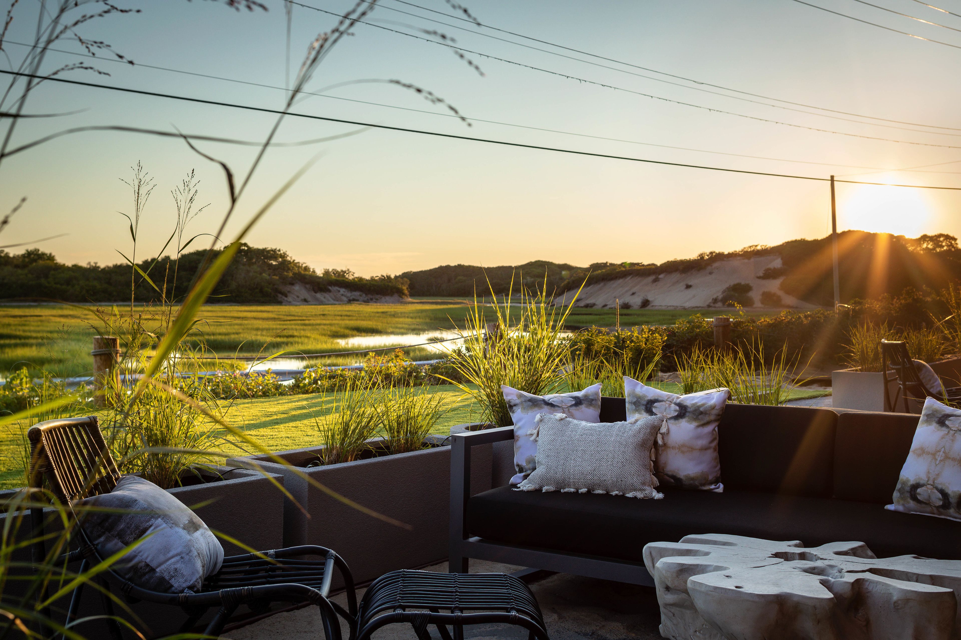 A patio with a sofa and chairs, overlooking a field and a sunset.