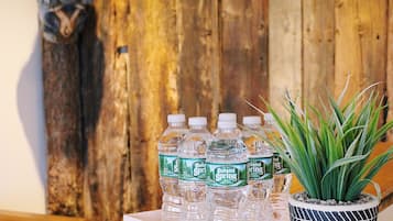 Una mesa de madera con una caja blanca que contiene botellas de agua Poland Spring, una planta en maceta y una silla de madera.