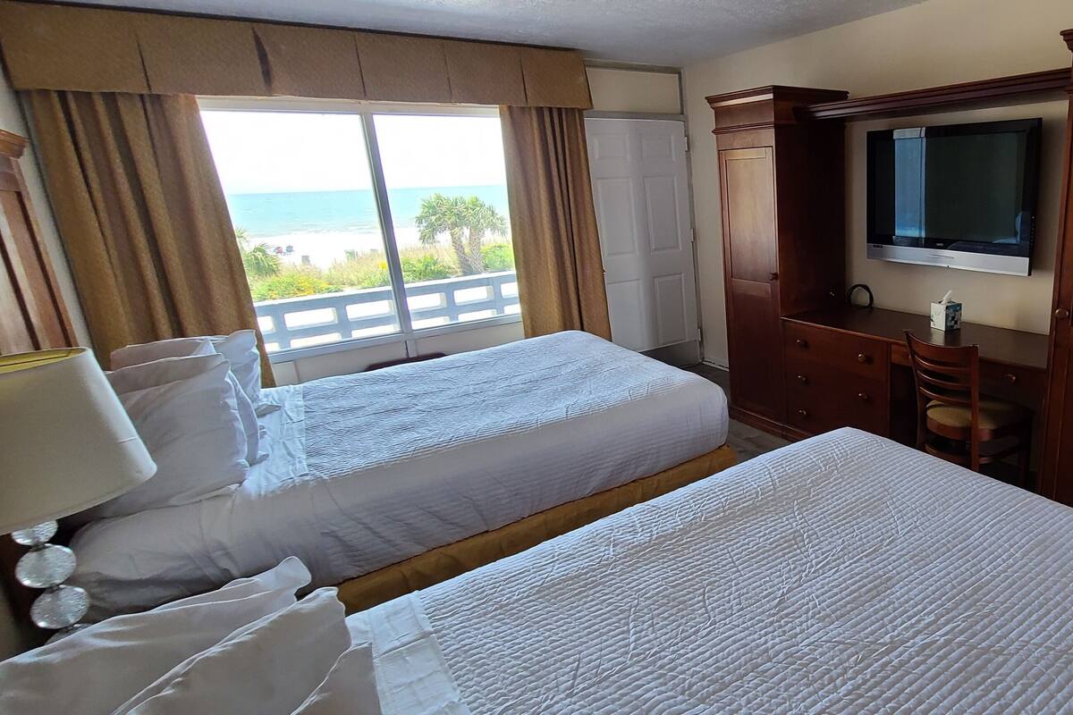 Une chambre d’hôtel avec deux lits, une télévision, un bureau avec une chaise et une vue sur la plage.