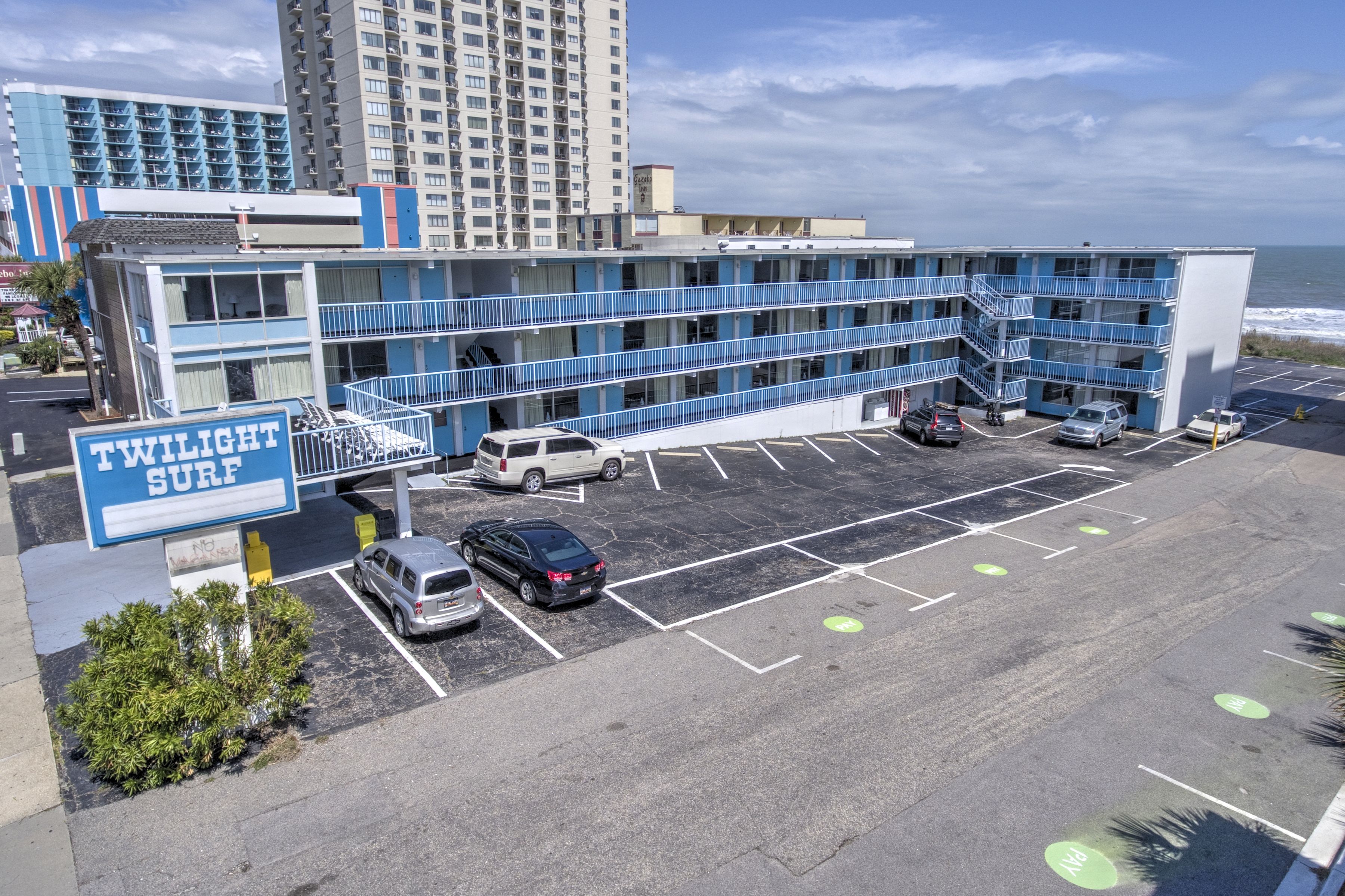 A multi-story motel with a sign reading "Twilight Surf" and a parking lot with several cars.