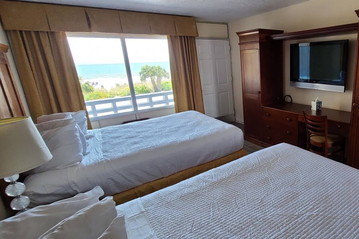 Une chambre d’hôtel avec deux lits, une télévision, un bureau et une fenêtre donnant sur la plage.
