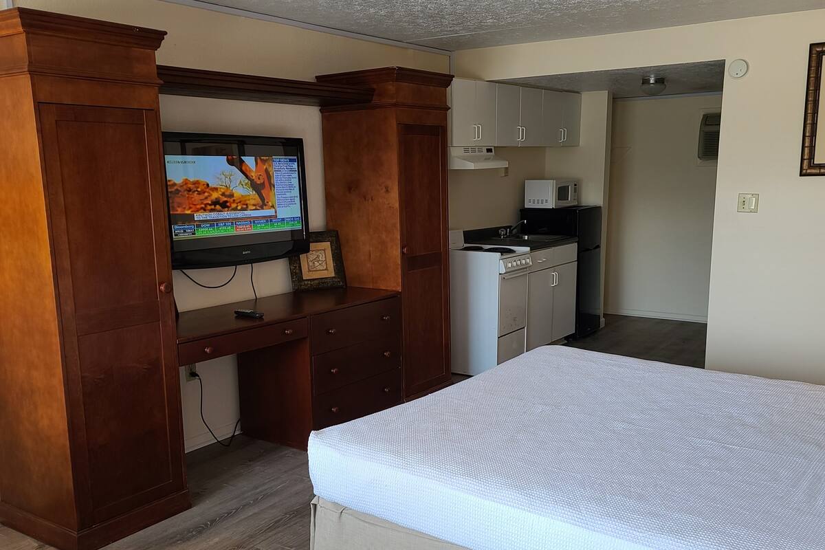 Une chambre de taille réduite comprenant un lit, un bureau avec une télévision, une kitchenette et une petite salle de bain.
