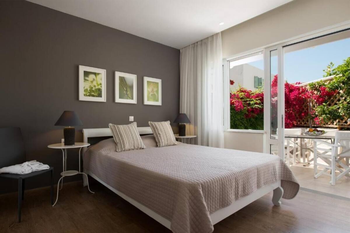 Un dormitorio moderno con una cama grande, dos mesitas de noche y vistas a un balcón con plantas y flores.