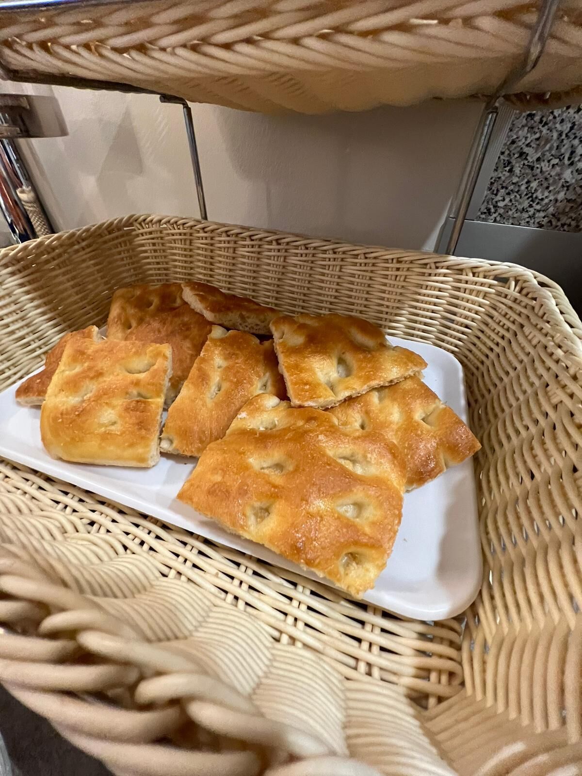 Una cesta con varias piezas horneadas de forma cuadrada y color marrón dorado, probablemente pan o pasteles, sobre un plato rectangular blanco.