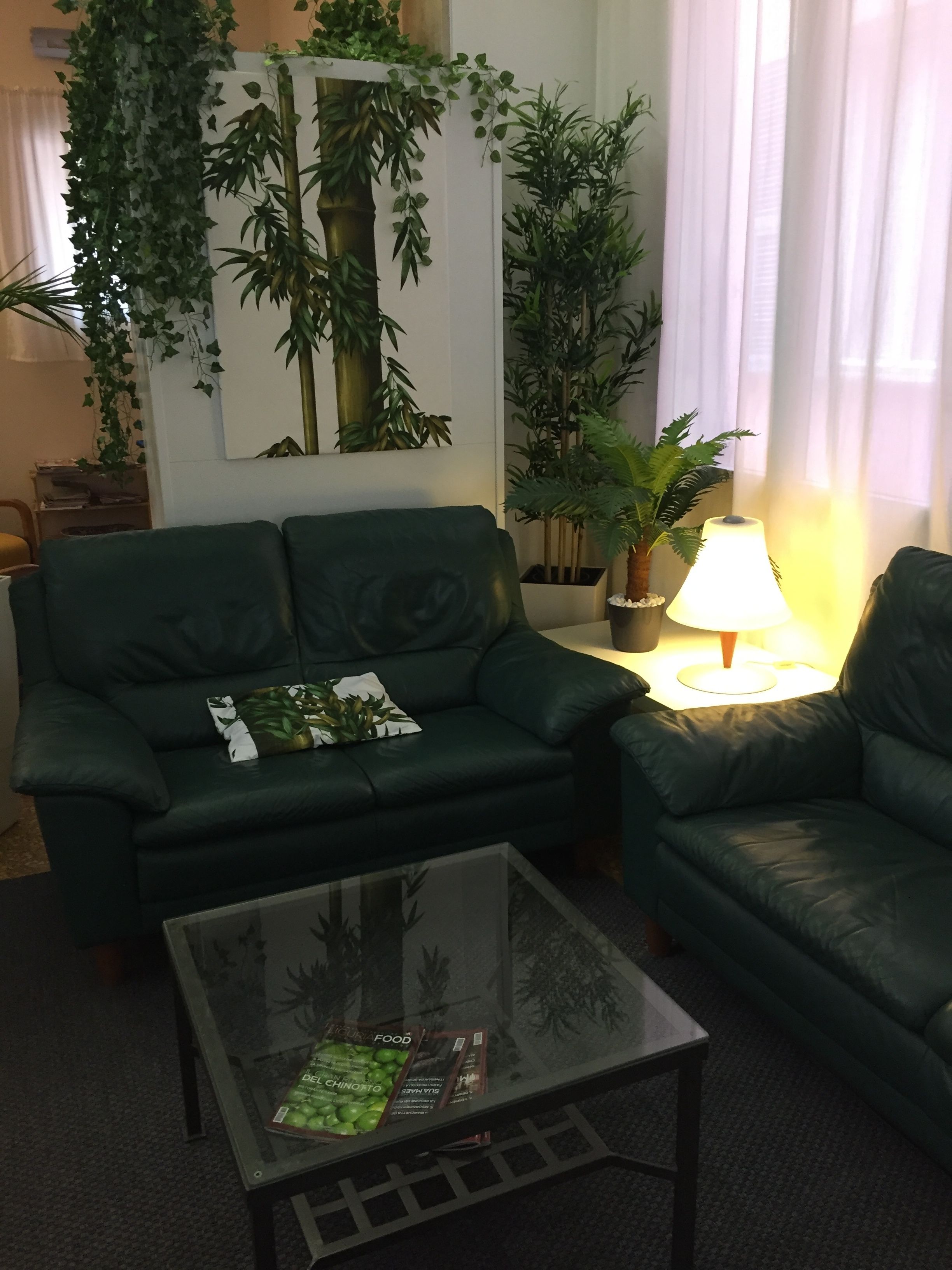 A living room with a green sofa, a glass coffee table with magazines, and a lamp.