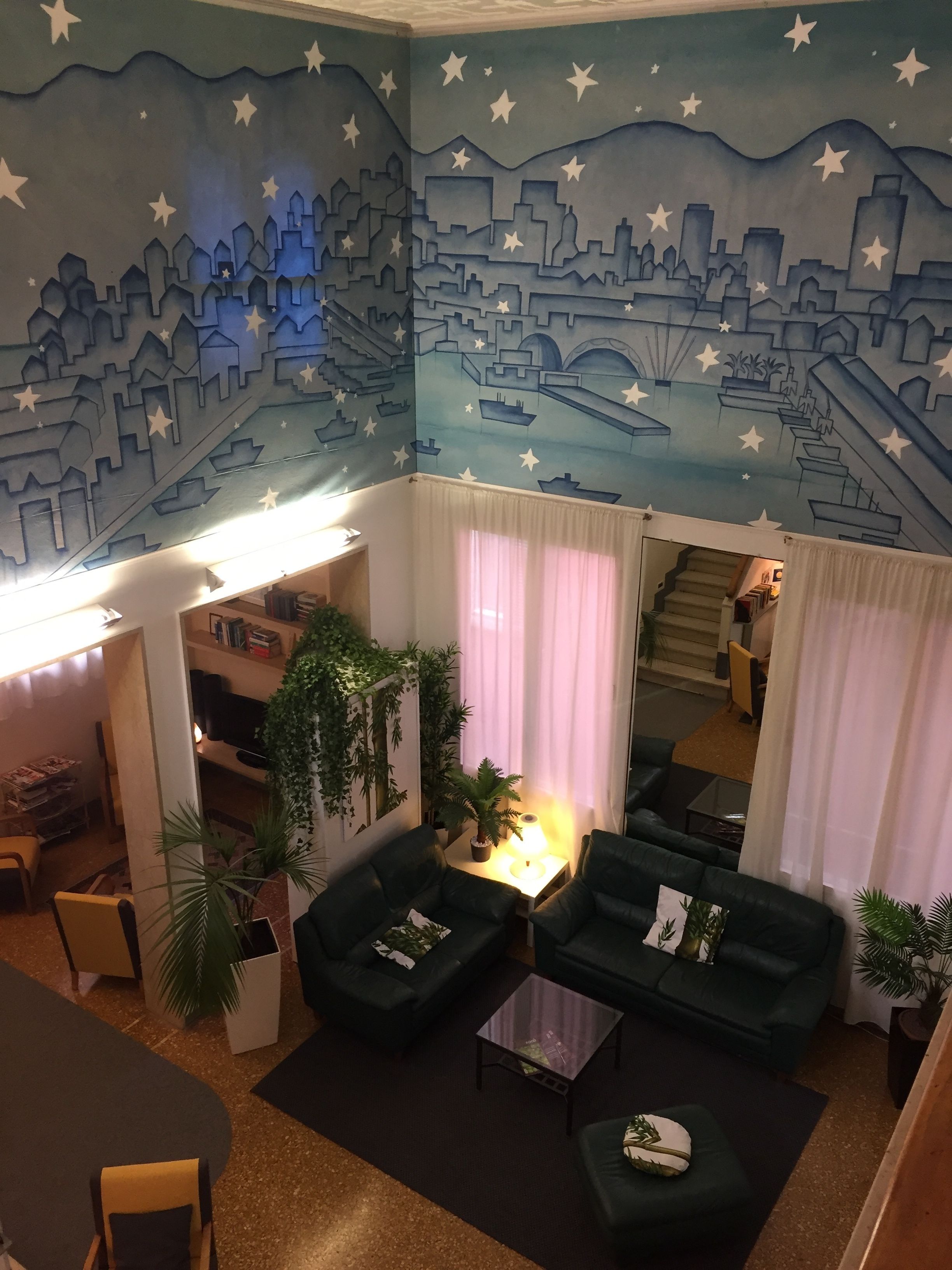 Un salon chaleureux avec une fresque représentant un paysage urbain peinte au plafond, une cheminée et des fauteuils confortables.