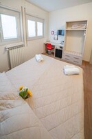 Una habitación de hotel con cama, escritorio, silla, radiador y armario.