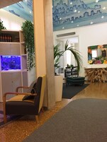Una habitación con una silla de madera, una estantería, un acuario pequeño, una planta, un escritorio y un espejo con diseño floral.