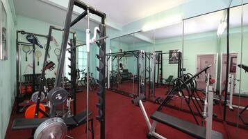 Un gimnasio con diverso equipo de ejercicio, incluyendo máquinas de pesas y pesas libres, y espejos en las paredes.