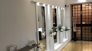 A reception area with a white reception desk, a mirror, and a series of white vases with flowers. - Hotel Cairoli (Genoa)