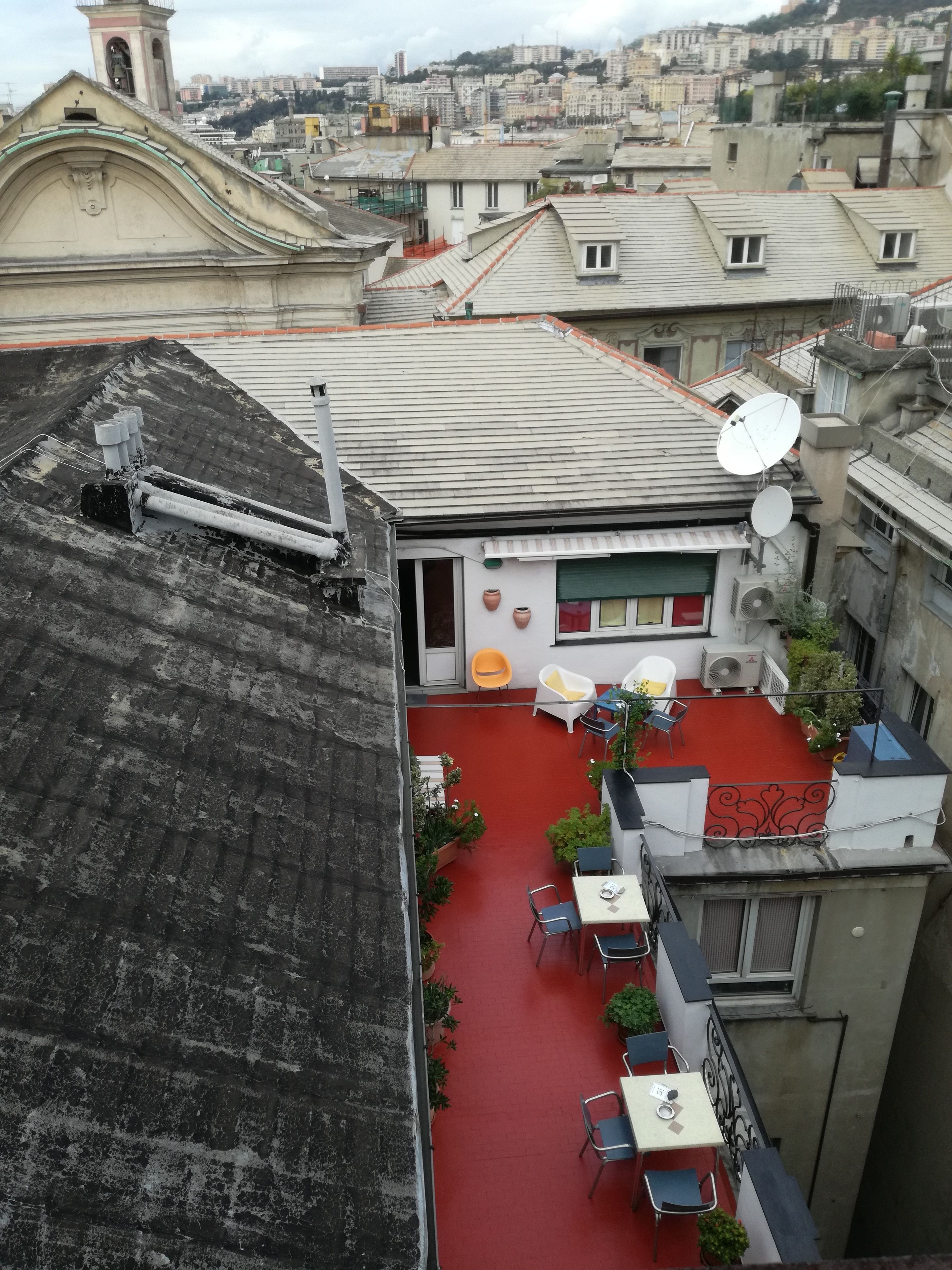 Eine Dachterrasse mit rotem Boden, weißen Wänden und einer kleinen Gartenanlage mit Blumentöpfen.