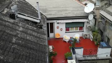 Eine Dachterrasse mit rotem Boden, weißen Wänden und einer kleinen Gartenanlage mit Blumentöpfen.