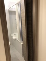 A narrow hallway leading to a bathroom with a shower, a towel rack, and a wooden door.