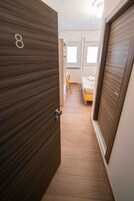 Een gang die leidt naar een slaapkamer met een bed, een stoel en een radiator.