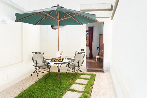 A patio with a table and chairs, an umbrella, and a small garden area. - Hotel Terranobile Metaresort (Bari)