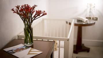 A white crib in a room with a small table and a vase of red flowers.