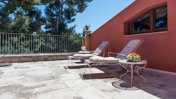 Una terraza con dos tumbonas y una mesa, rodeada por un muro rojo y una barandilla de metal.