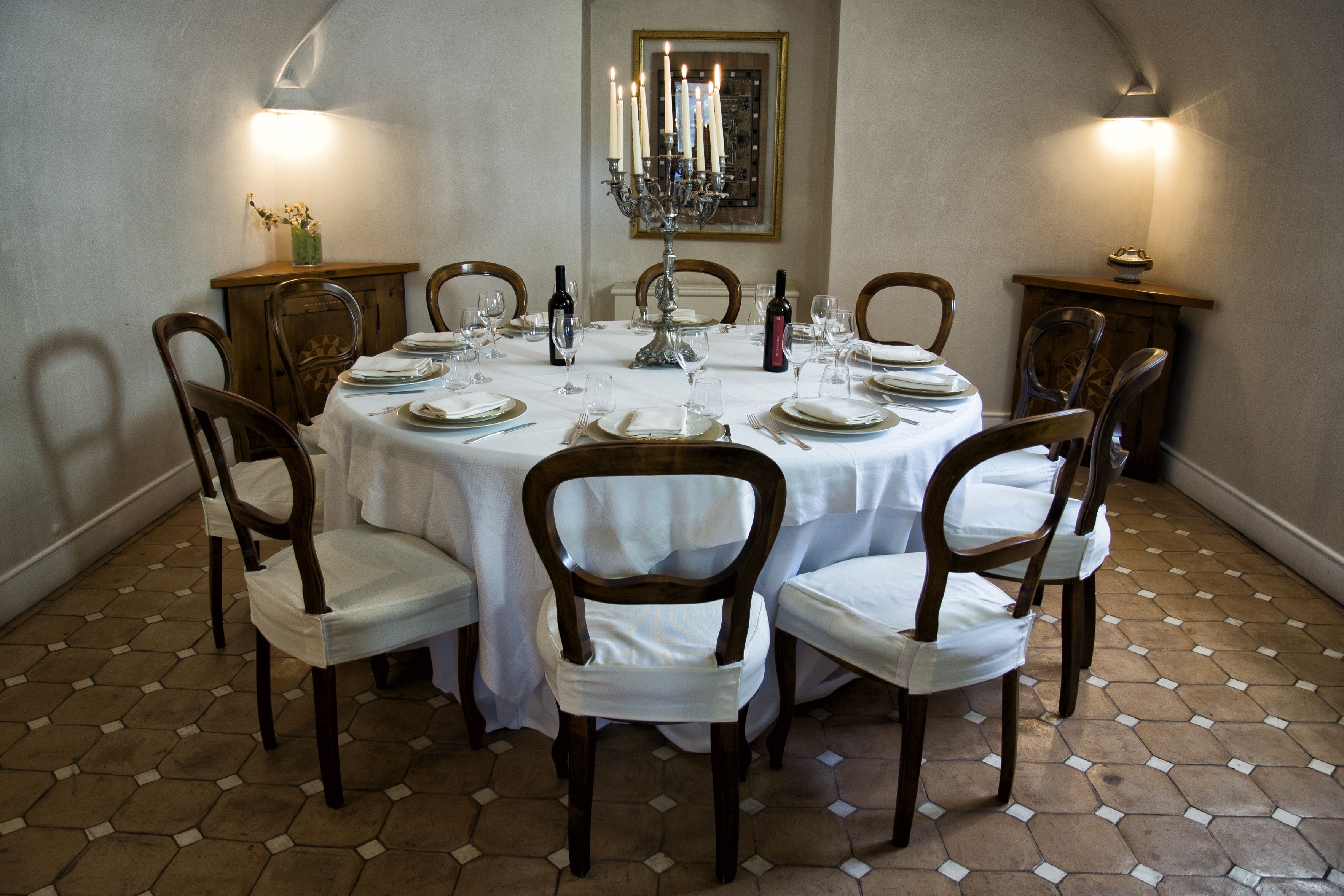 A dining room with a round table set for six, surrounded by wooden chairs with white cushions.