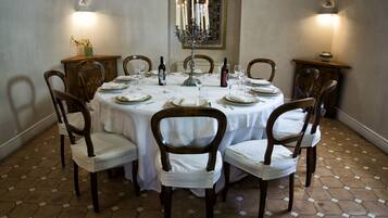 A dining room with a round table set for six, surrounded by wooden chairs with white cushions.