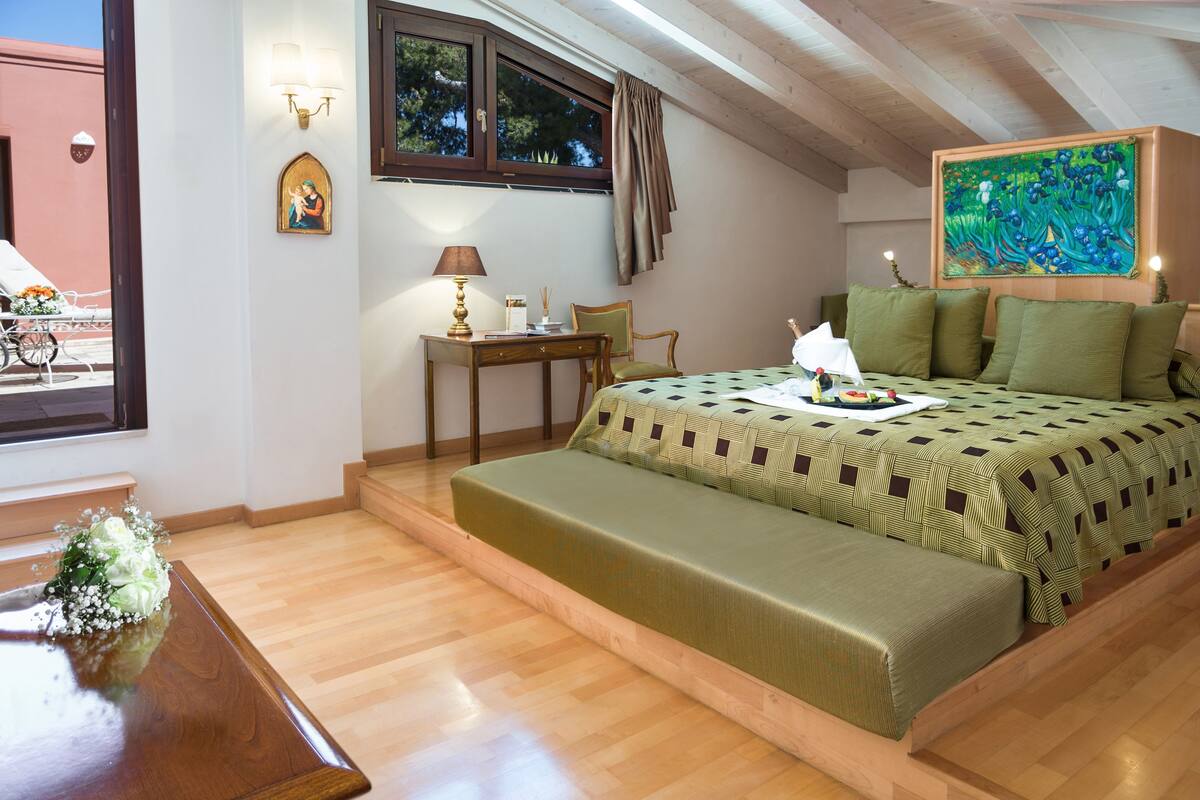 A bedroom with a bed, a desk, a chair, a window, and a painting.