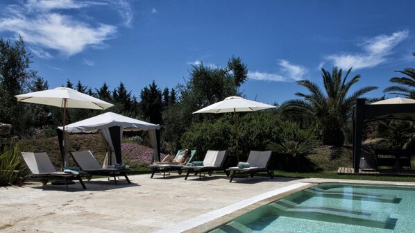 A poolside area with lounge chairs and umbrellas, surrounded by trees and a clear sky. - Hotel Terranobile Metaresort (Bari)
