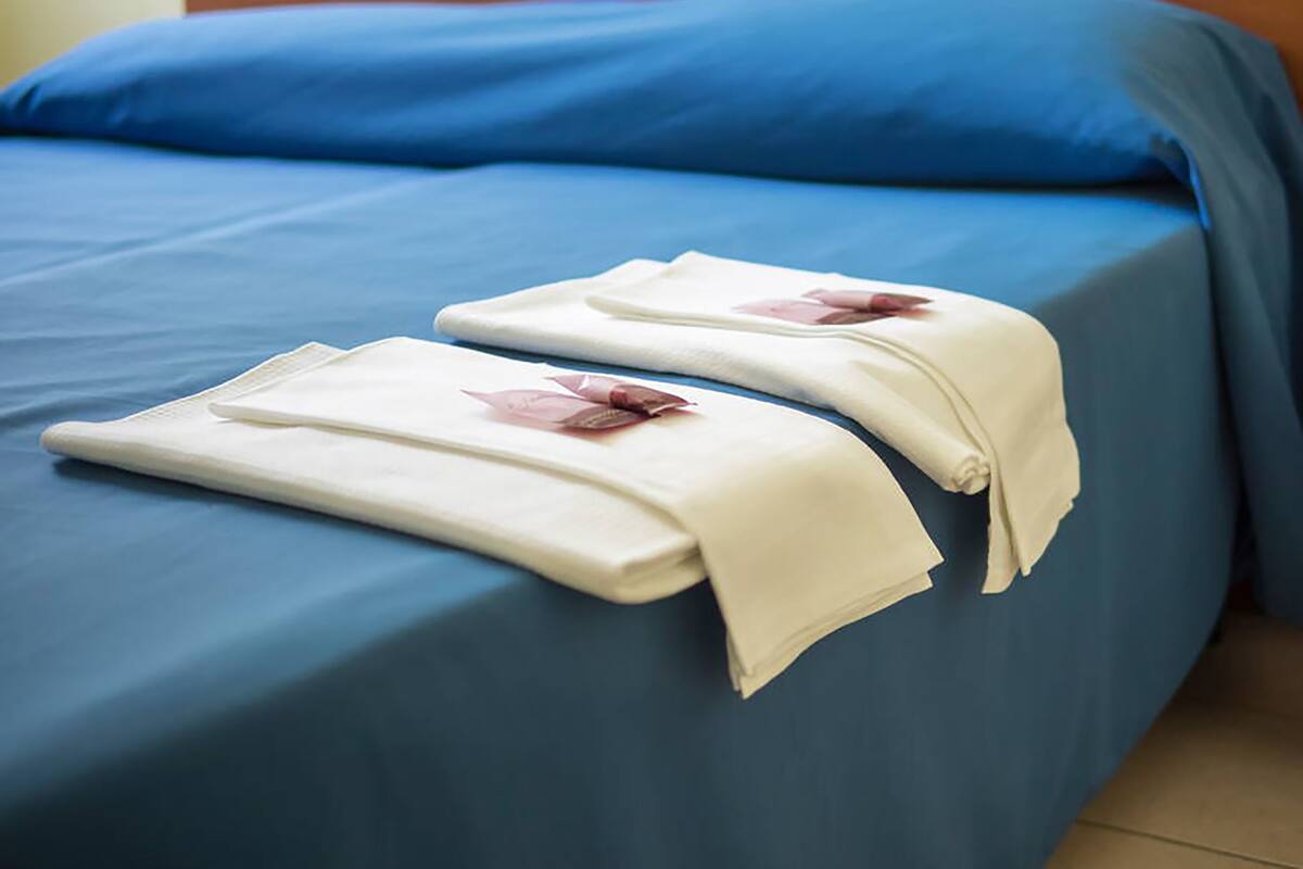 Ein Bett mit blauer Bettdecke und zwei gefalteten weißen Handtüchern mit rotem Logo.