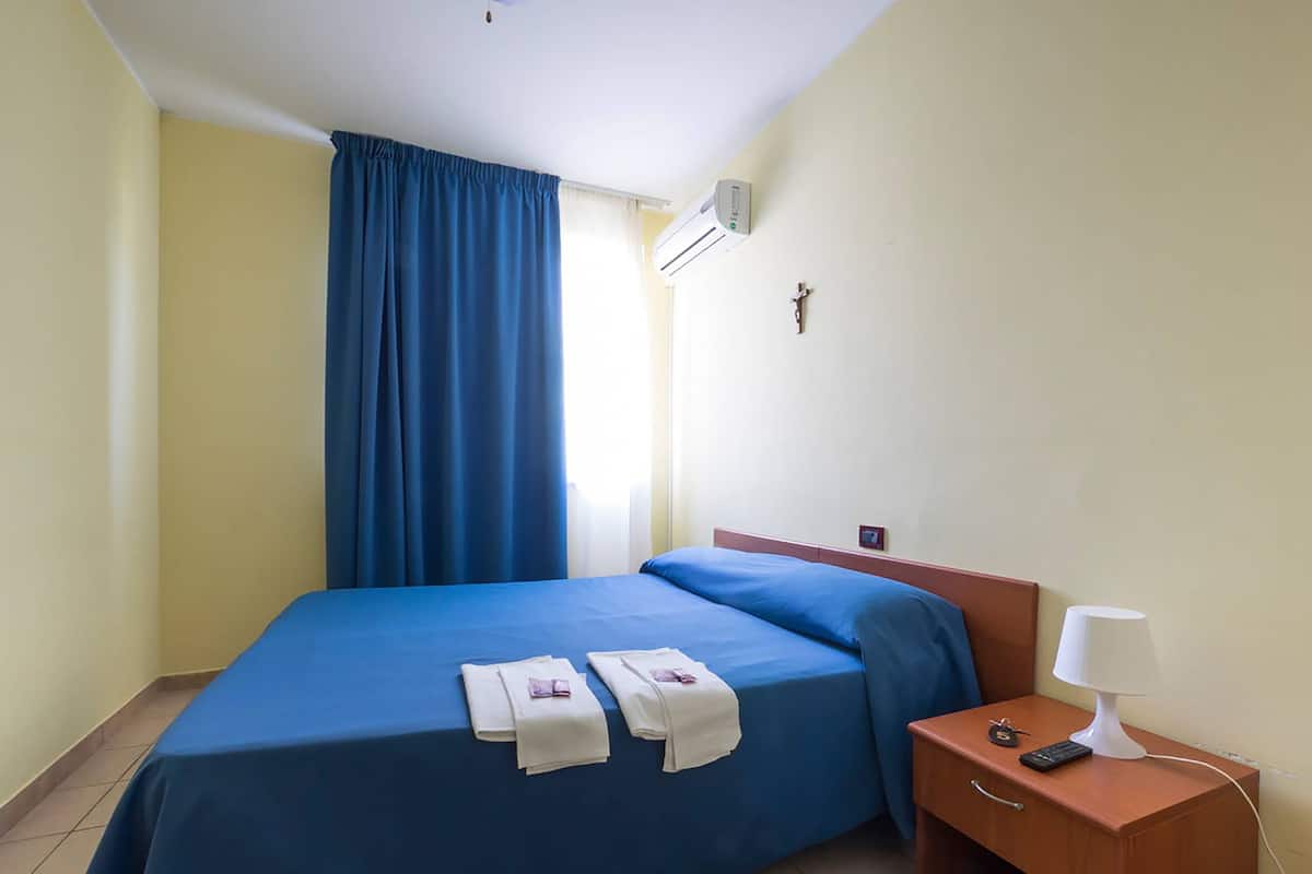 Ein Hotelzimmer mit einem Bett, einem Nachttisch mit Lampe und einem Fenster mit blauen Vorhängen.