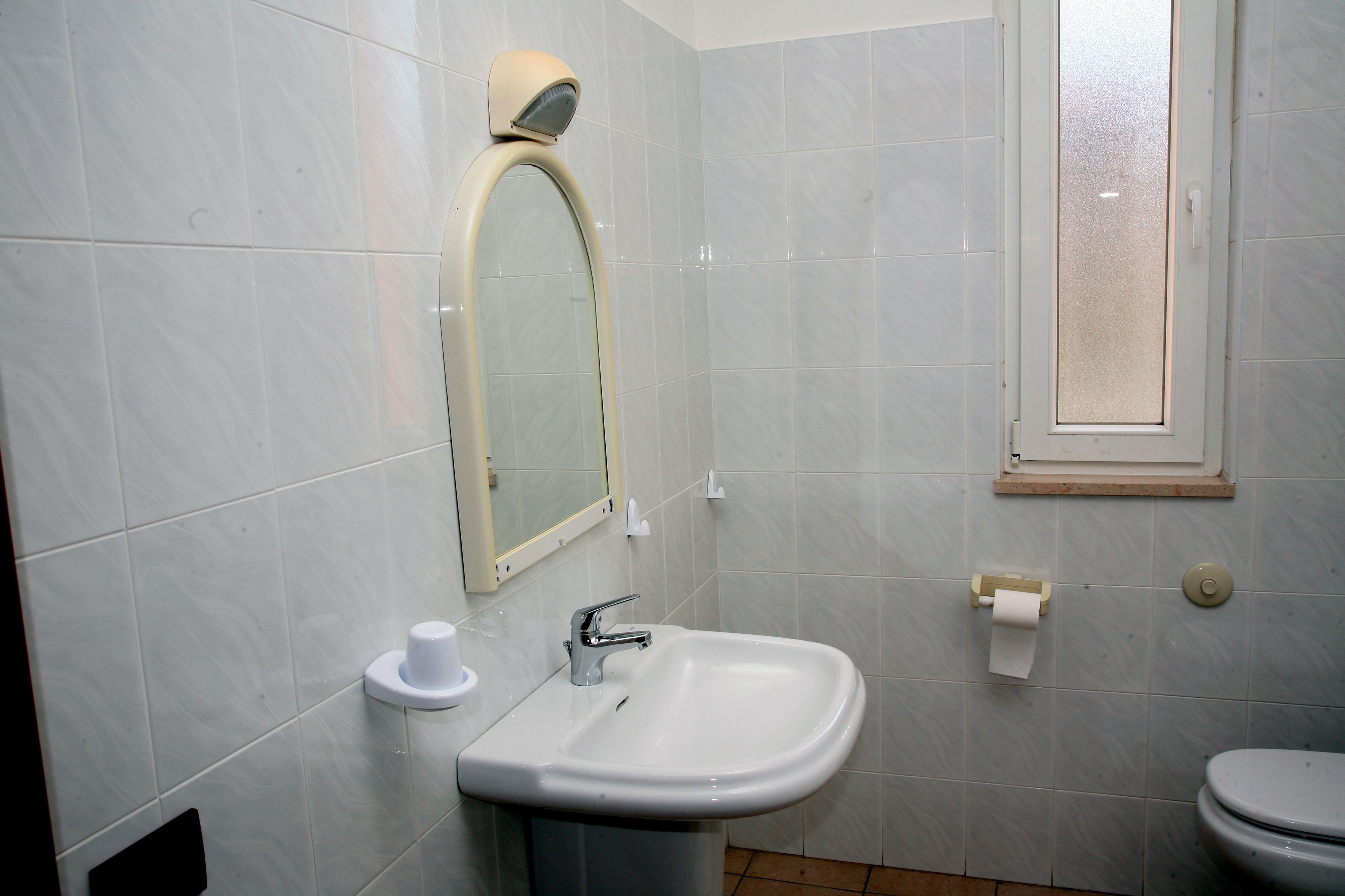 Une salle de bain avec un lavabo blanc, un miroir, des toilettes et une fenêtre.