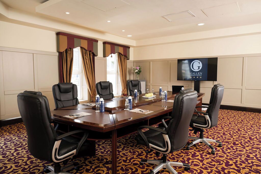 Un salón de conferencias con una larga mesa, seis sillas y una pantalla de televisión que muestra el nombre del hotel.