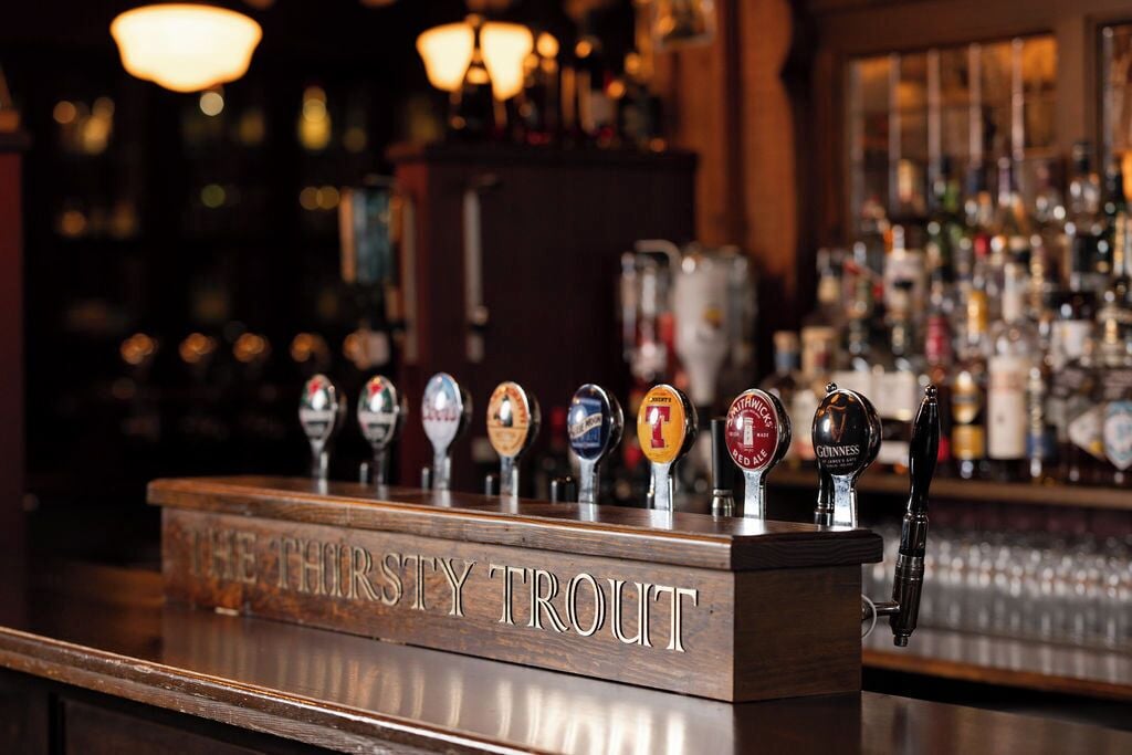 Un bar con múltiples grifos de cerveza y un letrero que dice "THE THORSTY TROUT".