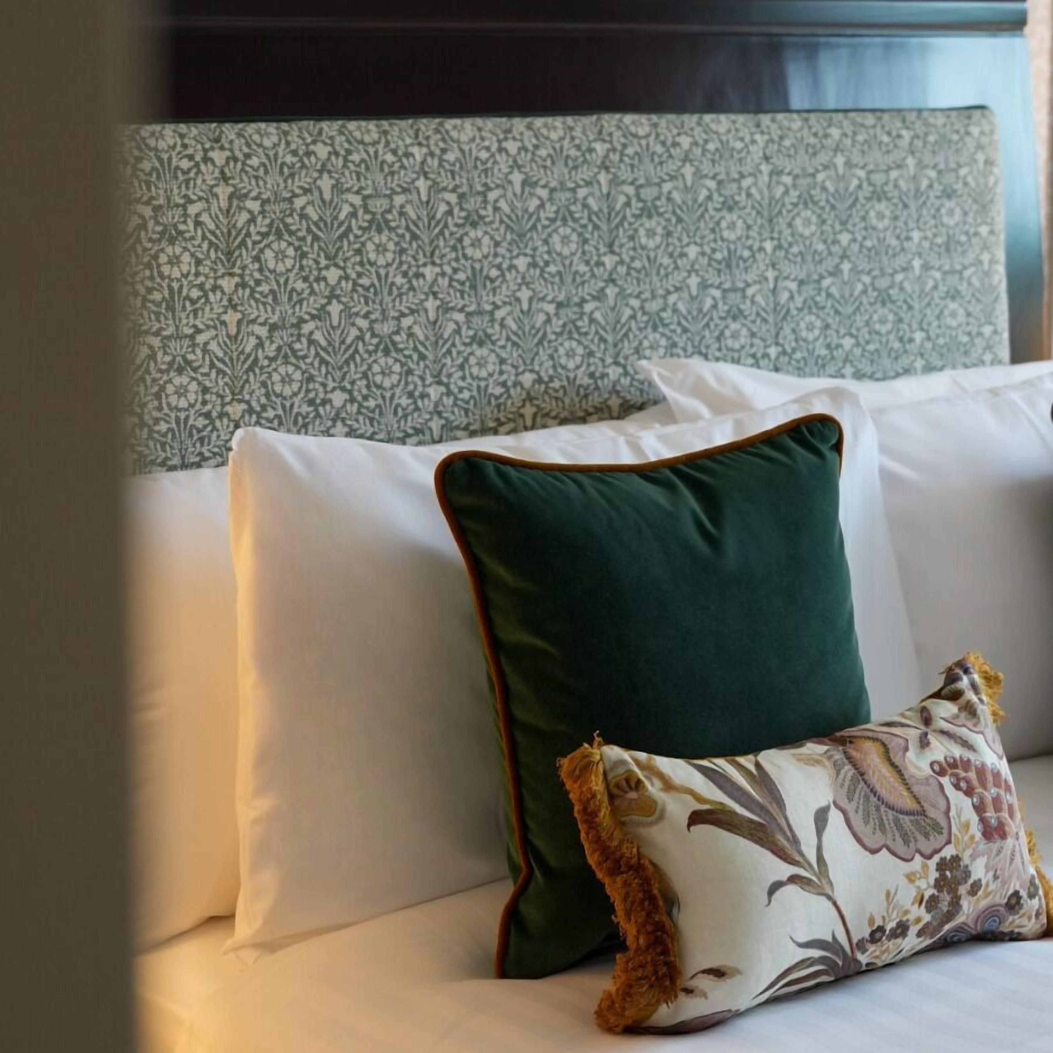 A bed with white and green pillows, a patterned pillow, and a dark headboard.