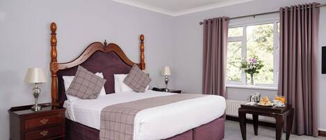 A bedroom with a large bed, two bedside tables, a window with curtains, and a small table with breakfast items.