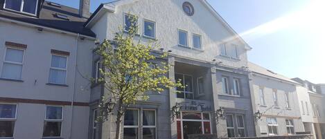 A two-story building with a stone facade, multiple windows, and a small tree in front.
