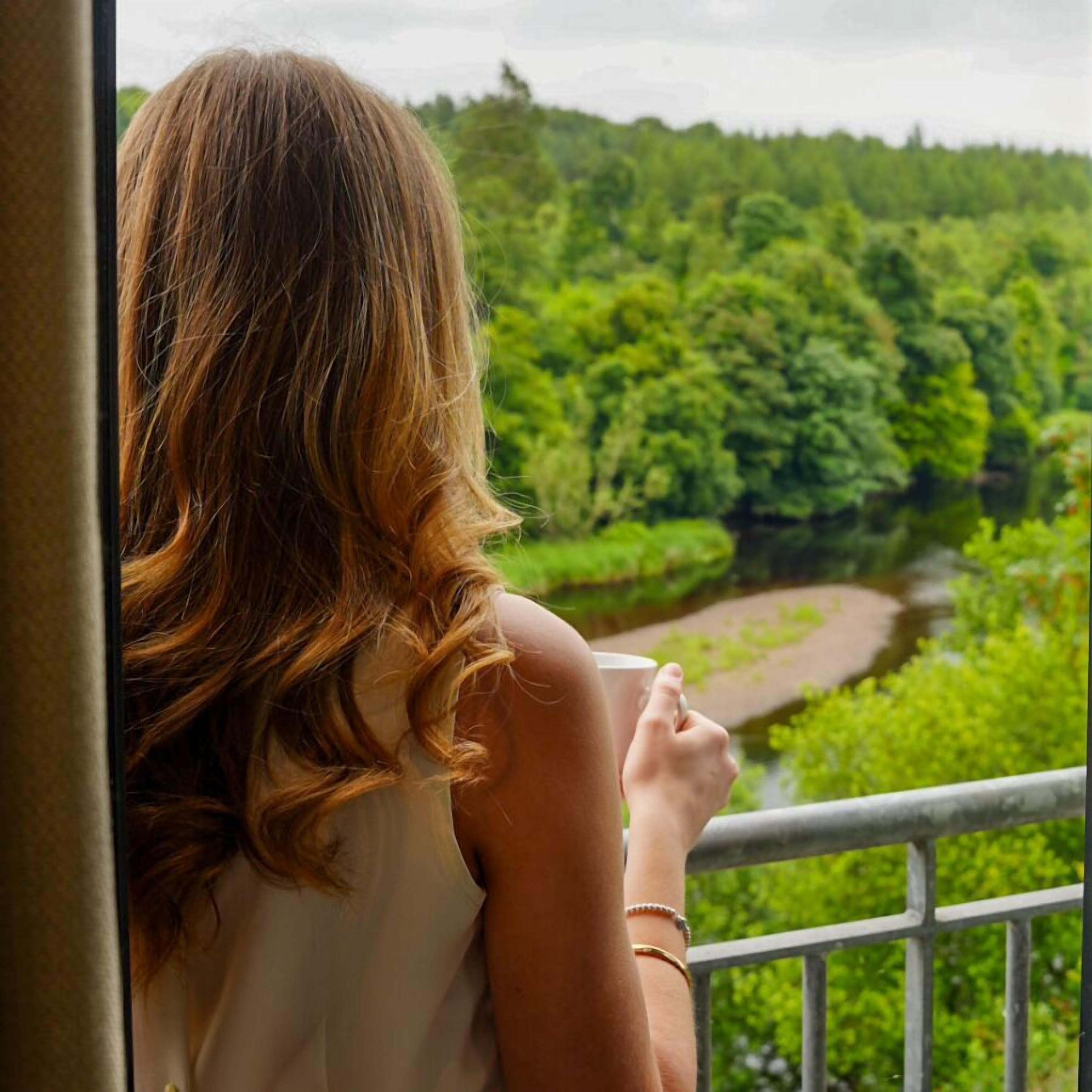 Una persona de cabello largo contemplando un exuberante paisaje verde con un río.