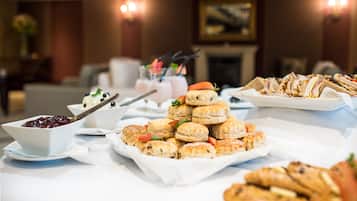 A buffet table with various food items including sandwiches, scones, and a bowl of fruit salad.