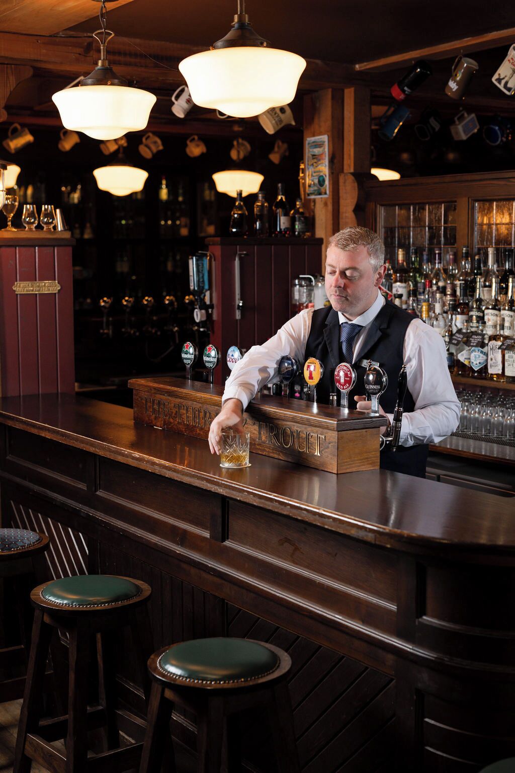 A bartender at a bar with multiple beer taps and a wooden counter.
