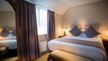 A hotel room with a large bed, a bedside table with a lamp, a mirror, and a window with curtains.