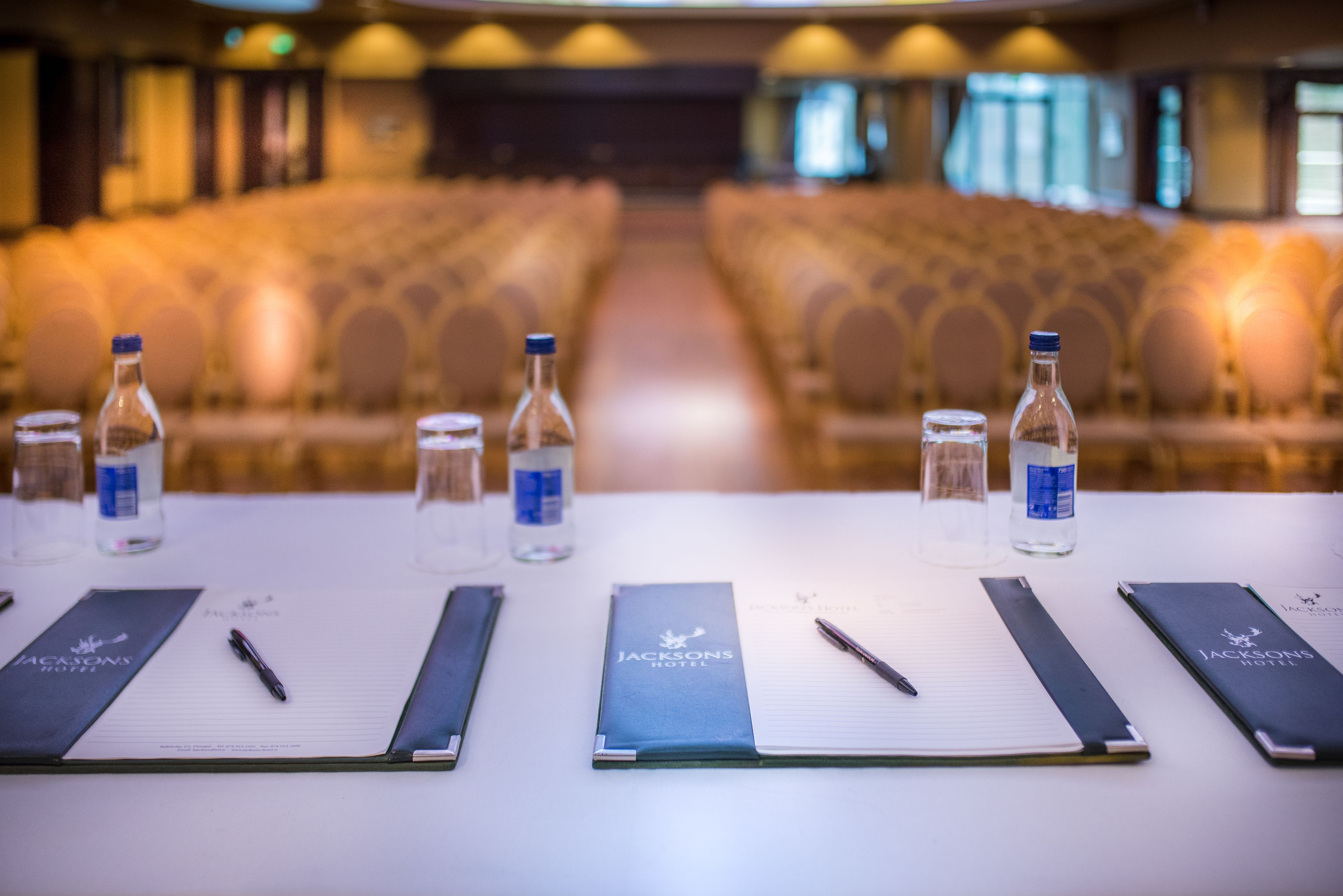 A conference room with rows of chairs, water bottles, notepads, and pens on a table.