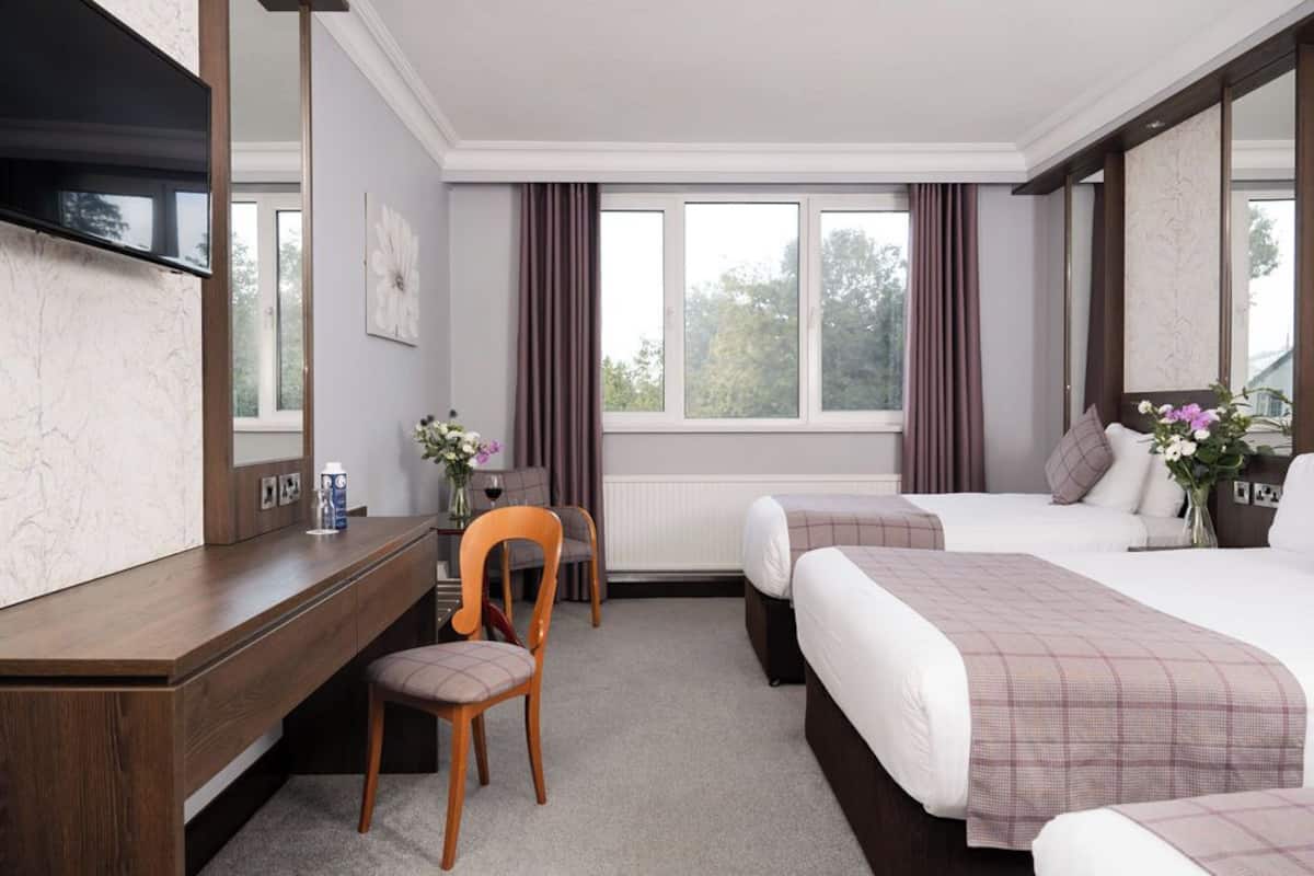Une chambre d’hôtel équipée d’un bureau, de deux lits, d’une grande fenêtre avec des rideaux et d’un miroir.