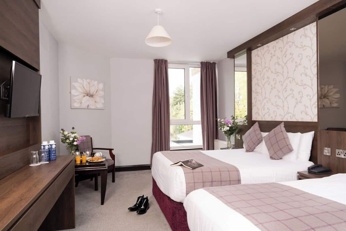 Une chambre d’hôtel avec deux lits, un bureau avec une télévision, une chaise et une fenêtre avec des rideaux.
